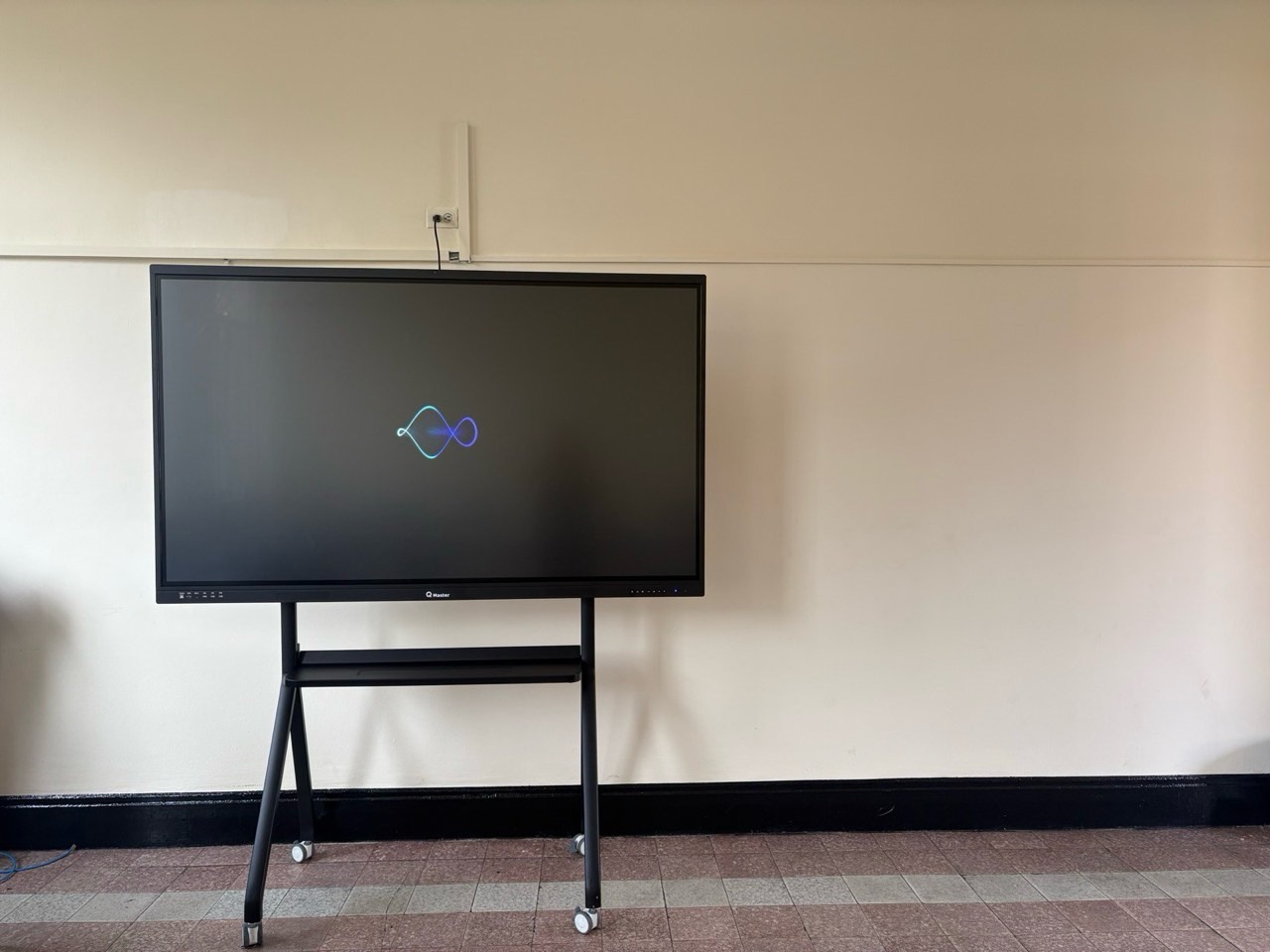 Pantalla interactiva QMaster en soporte móvil contra una pared del aula