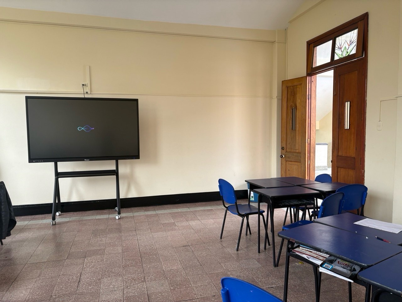 Aula de colegio con pantalla interactiva en soporte móvil frente a los pupitres