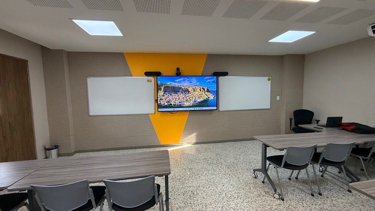 Aula híbrida con pantalla interactiva, cámara y dos barras de sonido sobre la pared
